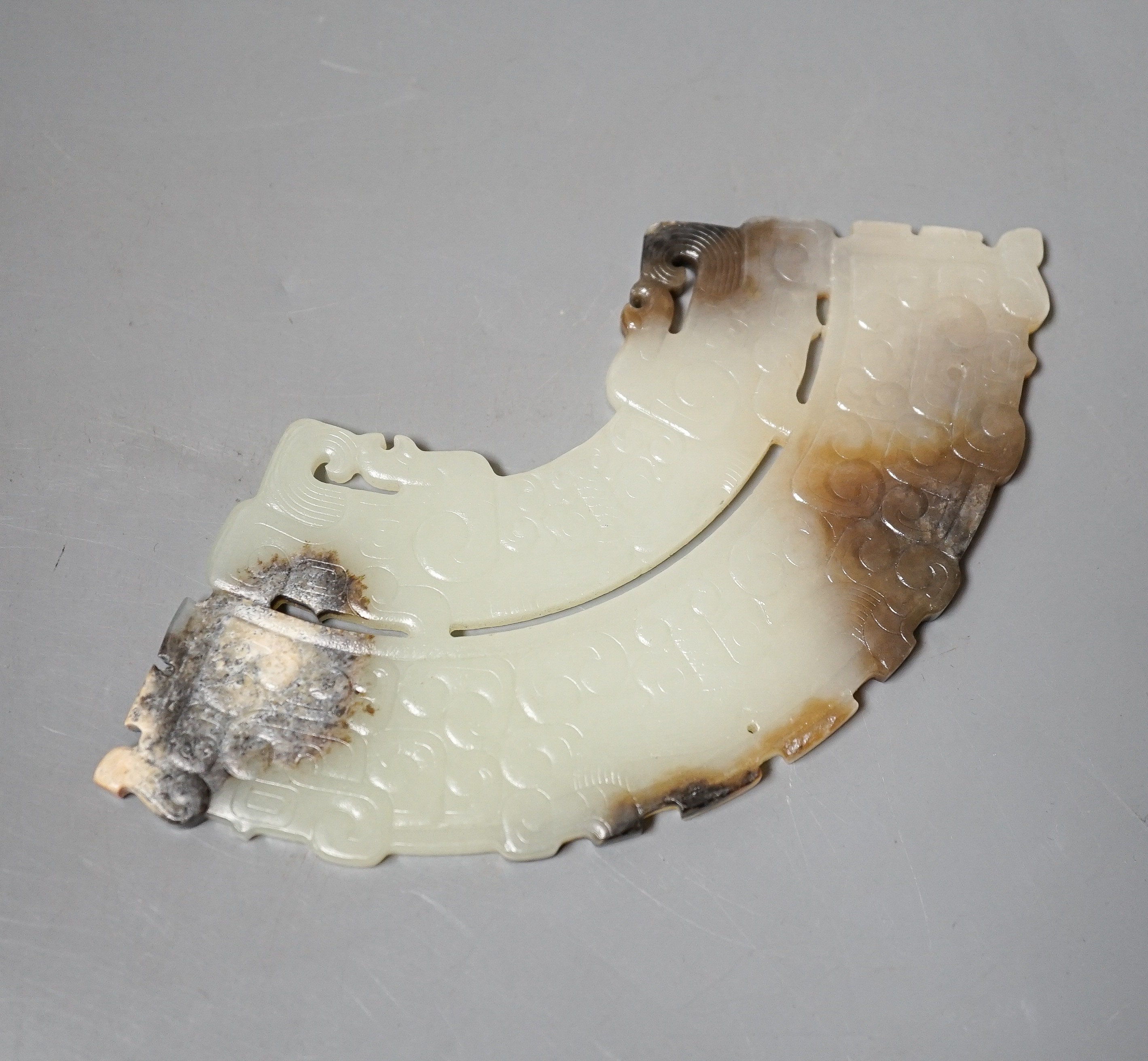 A Chinese archaistic jade fan shaped plaque, the pale celadon stone with brown and black inclusions, carved in low relief with taotie masks and leiwen, width 14.7cm